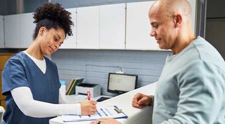 a dental front desk worker helping a patient fill out forms