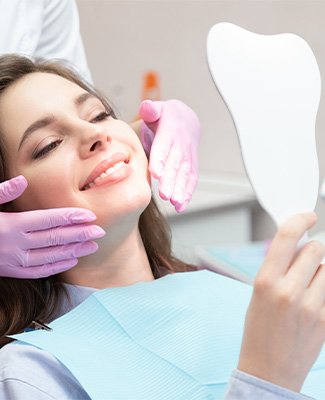 Woman in dental chair smiling at results in handheld mirror