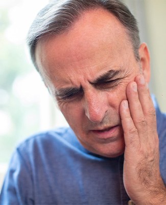 Man in blue shirt touching hand to jaw in pain
