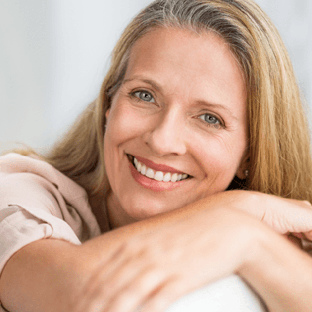 A mature and smiling woman sitting on a couch 