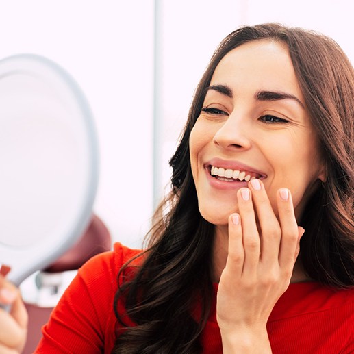 A woman admiring her new dental implant in a hand mirror