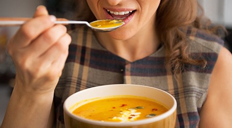 A young woman eating pumpkin soup in her kitchen