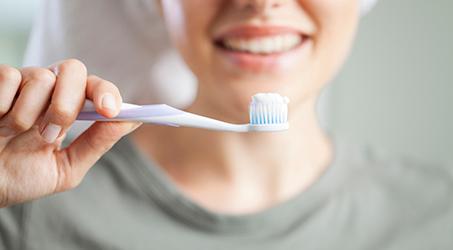 A closeup of a toothbrush with toothpaste and a blurred person in the background