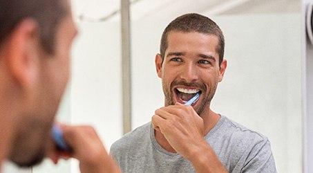 Handsome man brushing his teeth in front of bathroom mirror