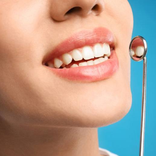 Close up of a dental mirror next to a patient’s smile