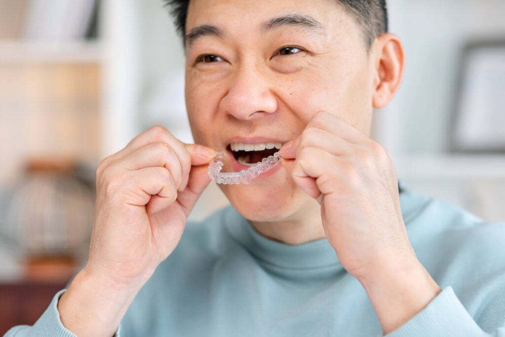 Man smiling while putting on clear aligner